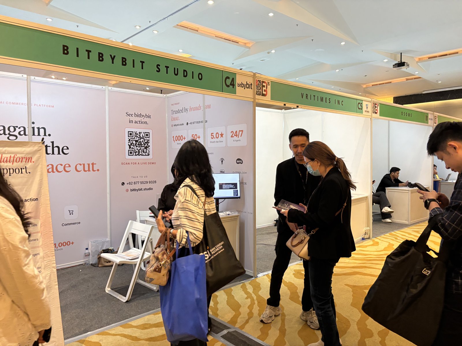 bitbybit team members at the B2B Tech Asia 2026 booth, walking a visitor through the conversational commerce demo on a laptop