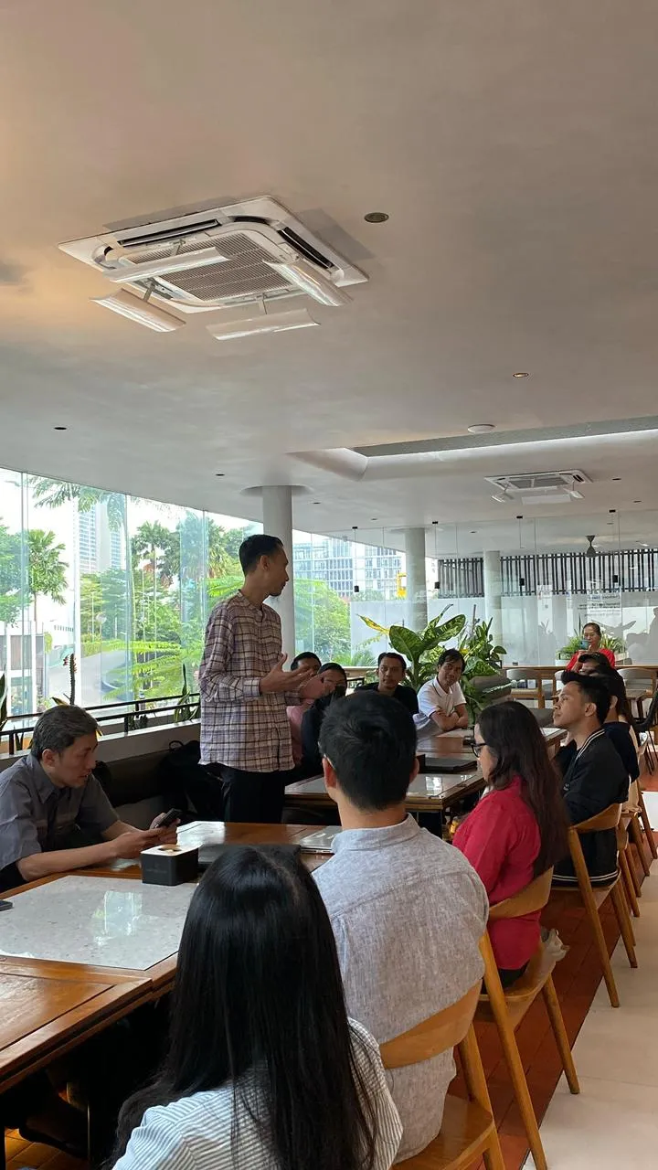 Host standing and presenting to attendees seated around tables at the Executive Iftar 2026 in Jakarta